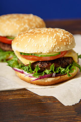 Classical burger with beef patty, tomatoes, cheese, onion, cucumber and lettuce served on wooden table against blue background
