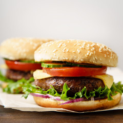 Classical burger with grilled meat, tomatoes, cheese, onion, cucumber and lettuce served on wooden table