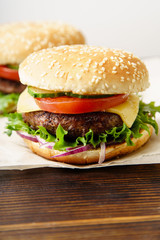 Classical burger with grilled meat, tomatoes, cheese, onion, cucumber and lettuce served on wooden table