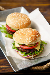 Classical burger with beef patty, tomatoes, cheese, onion, cucumber and lettuce served on wooden table