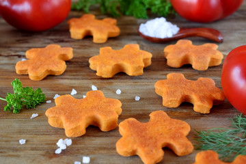Puzzle shaped salty cookies with paprika and tomato paste on a wooden board surrounded by the ingredients
