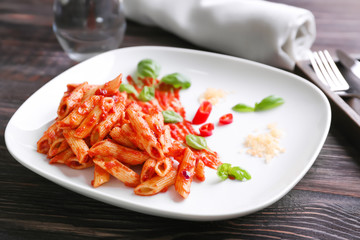 Plate with delicious penne pasta and sauce on table