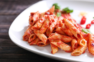 Plate with delicious penne pasta and sauce on table, closeup