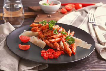 Plate with delicious penne pasta and garnish on table