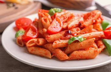 Plate with delicious penne pasta and garnish on table, closeup