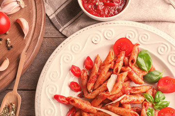Plate with delicious penne pasta and garnish on table