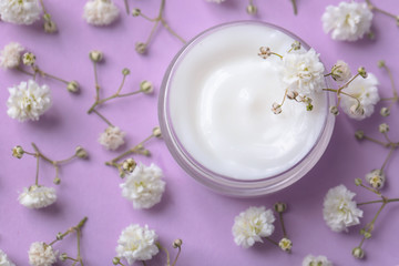 Obraz na płótnie Canvas Jar of body cream and beautiful flowers on color background