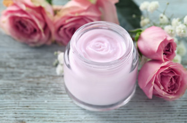 Obraz na płótnie Canvas Jar of body cream and beautiful flowers on wooden background
