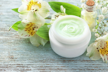 Fototapeta na wymiar Jar of body cream and beautiful flowers on wooden background