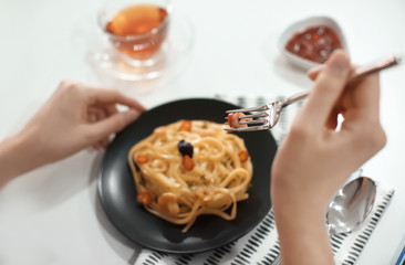 Young woman eating tasty pasta at table