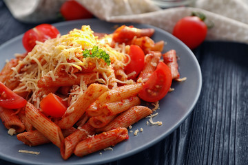 Plate of tasty penne pasta with tomato sauce on wooden table, closeup