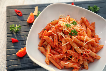 Plate of tasty penne pasta with tomato sauce on table