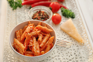 Bowl with tasty penne pasta and tomato sauce on table