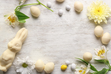 Beautiful Easter composition with chocolate bunny, eggs and flowers on wooden background, top view