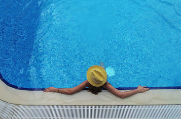 Young beautiful girl in yellow swimsuit and hat resting in the water closeup in swimming pool