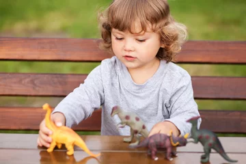 Selbstklebende Fototapeten Dinosaurier Toddler kid playing with a toy dinosaurs outdoors  © Alinsa