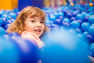 Happy little girl child in colourful blue plastic balls pool.