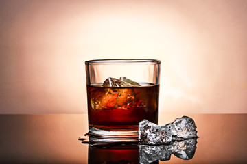 whiskey with ice on yellow background on a reflective glass base