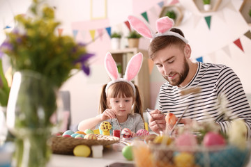 Father painting Easter eggs with his daughter at table