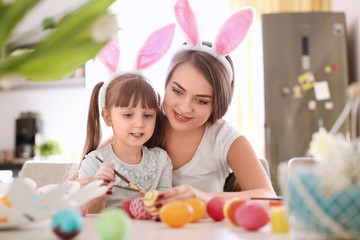 Mother painting Easter eggs with her child at table