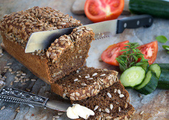 angeschnittener Brotlaib mit Butter, Gurke und Tomate zum belegen