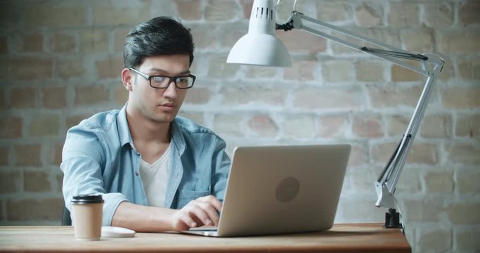 Young handsome asian businessman working at laptop in loft office dollyshot 4k