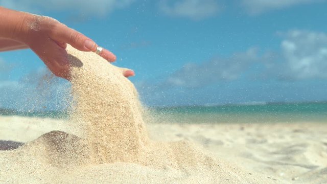 SLOW MOTION, CLOSE UP, COPY SPACE: Unknown young woman lets sand fall from her soft hands and back on the tranquil tropical shore. Summer wind scatters sand across the beautiful paradise island beach.