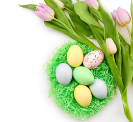 Decorative nest with dyed Easter eggs and spring flowers on white background