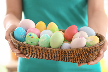 Fototapeta na wymiar Young woman with wicker bowl full of colorful Easter eggs, closeup