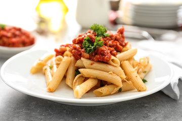 Plate with tasty penne pasta and bolognese sauce on table, closeup