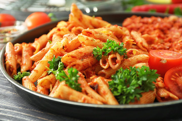 Frying pan with tasty penne pasta and tomato sauce on table, closeup
