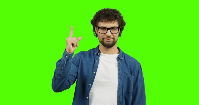 Young handsome man in the glasses and jeans shirt pointing up with his finger in the sky. Green screen. Chroma key.