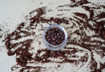 Coffee beans in a cup with coffee powder spread on the side
