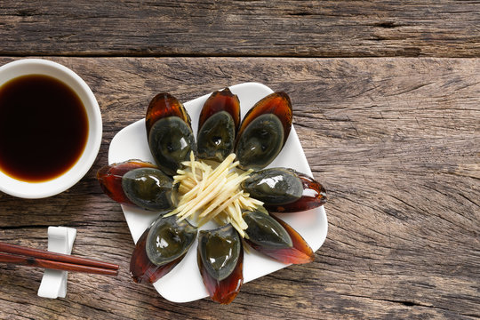 preserved egg in a ceramic plate served with soy sauce on old wooden table, copy space for text. delicious appetizer menu