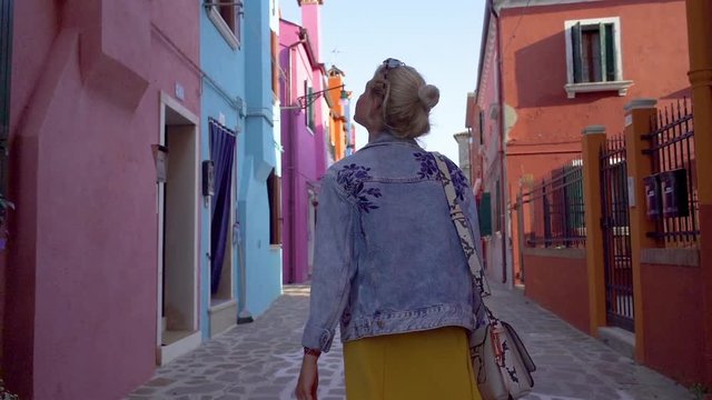 Young woman walking in colorful streets of Burano, Italy during sunset