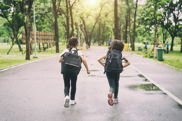 Two pupils of primary school run go to shool. Two girl with bags behind the back. Warm day of fall....