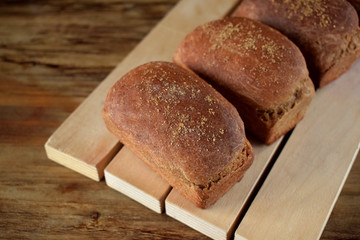 Loaves of rye bread sprinkled with coriander on a wooden board