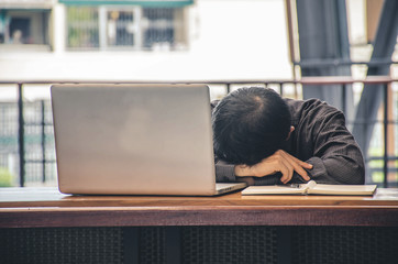 Tired businessman sleeping at his working place office with head on the desk near monitor of computer.