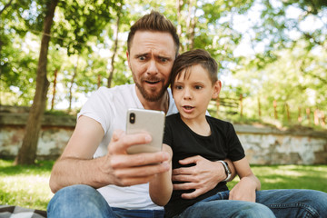 Shocked young father sitting with his little son using mobile phone.