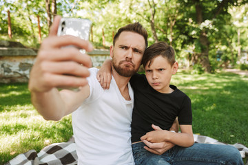 Funny young father sitting with his little son make selfie by mobile phone.