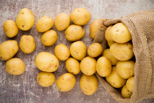 Sack of fresh raw potatoes on wooden background, top view.