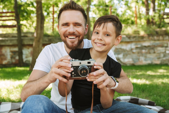 Young father sitting with his little son holding camera photographing.