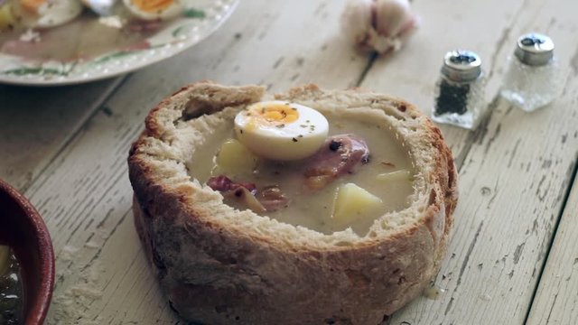Putting eggs on top of traditional soup called zur or white borscht into bread bowl