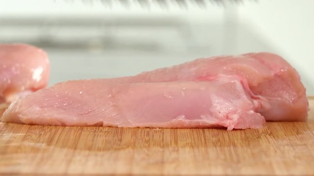 A woman pounds a chicken breast on a chopping board in a kitchen - closeup