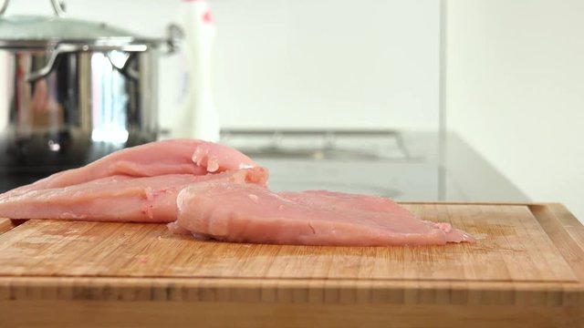 A woman pounds a chicken breast on a chopping board in a kitchen - closeup
