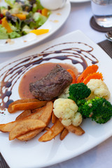 Beef steak brown sauce served with vegetable and fries in a nice dish.