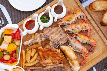 Meat platter served with salad, fries and red wine with three choice of sauce on wood block at fine dining table set.