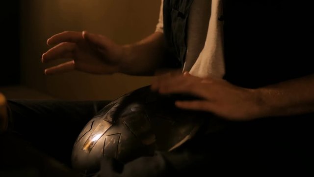 Man playing tank drum or hang at home. Warm romantic illumination, low key. Relaxation, meditative and traditional music concept. Close up shot