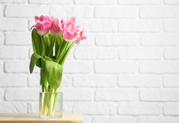 Vase with beautiful tulips against white brick wall