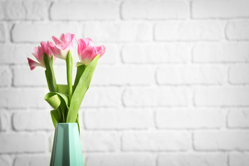 Vase with beautiful tulips against white brick wall